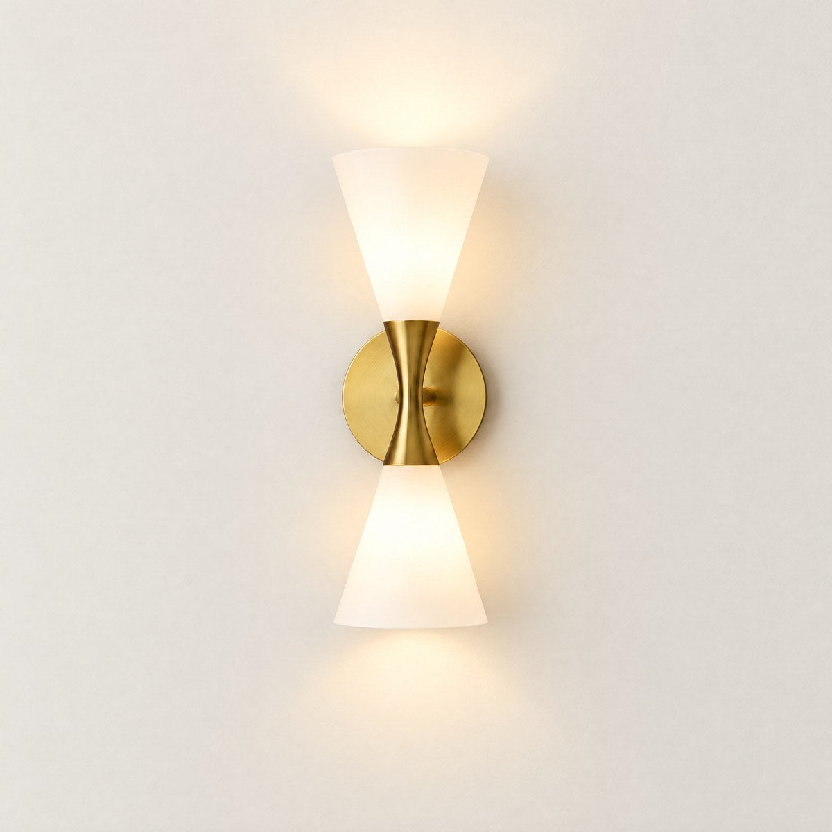Como hourglass wall light with frosted glass cones and gold frame, lit, on white wall