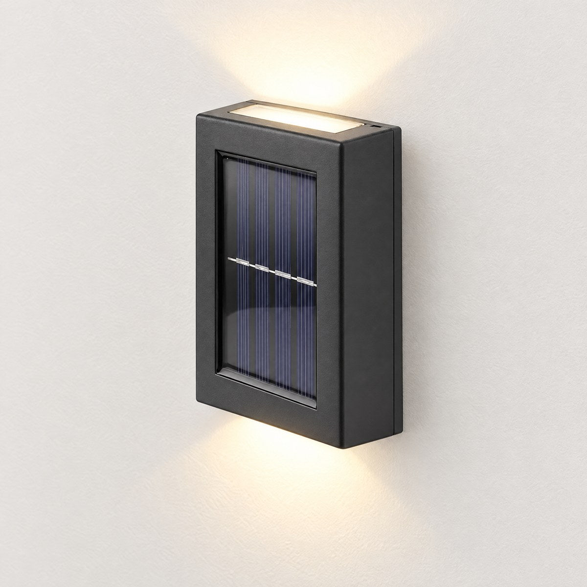 Glint black solar up and down wall light casting warm white light on a white wall