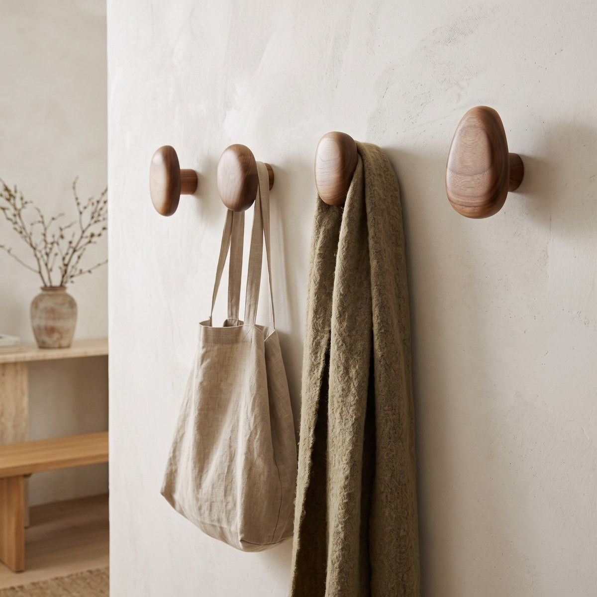 Kiyo walnut pebble hooks holding a linen tote and wool scarf in a limewashed hallway