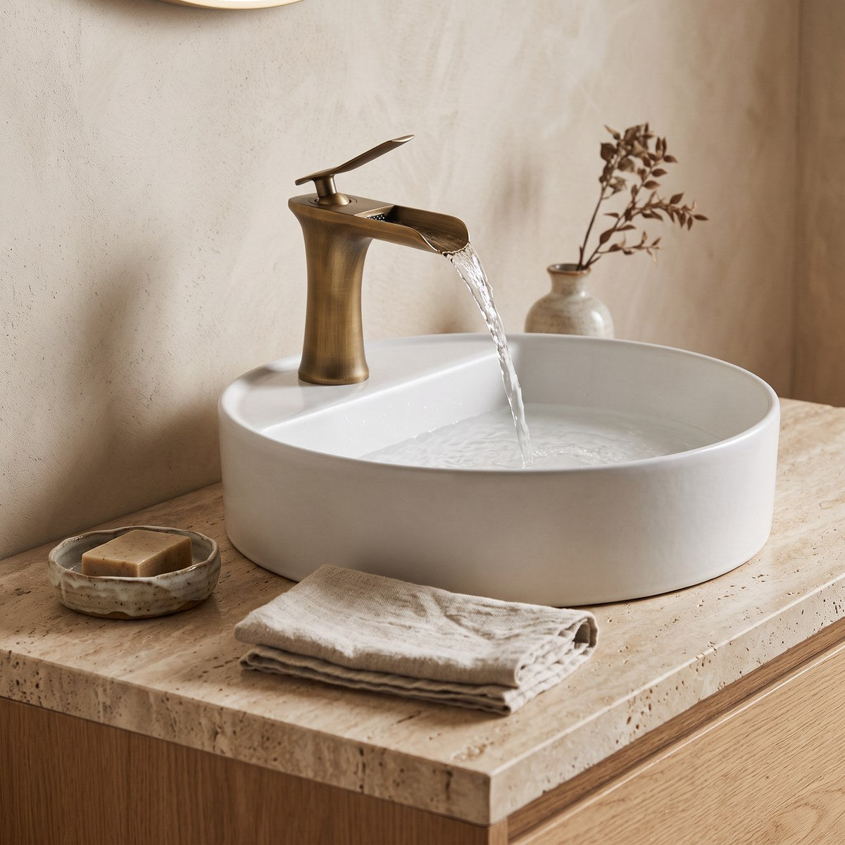 Nivexa vintage gold waterfall tap running into a white basin on a travertine vanity