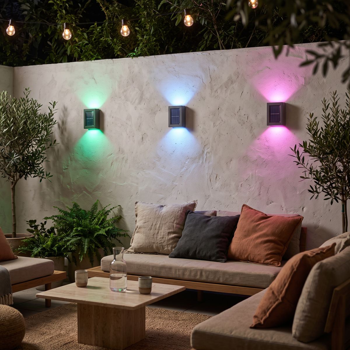 Glint colour-changing solar wall lights in green, blue and pink on a garden terrace wall