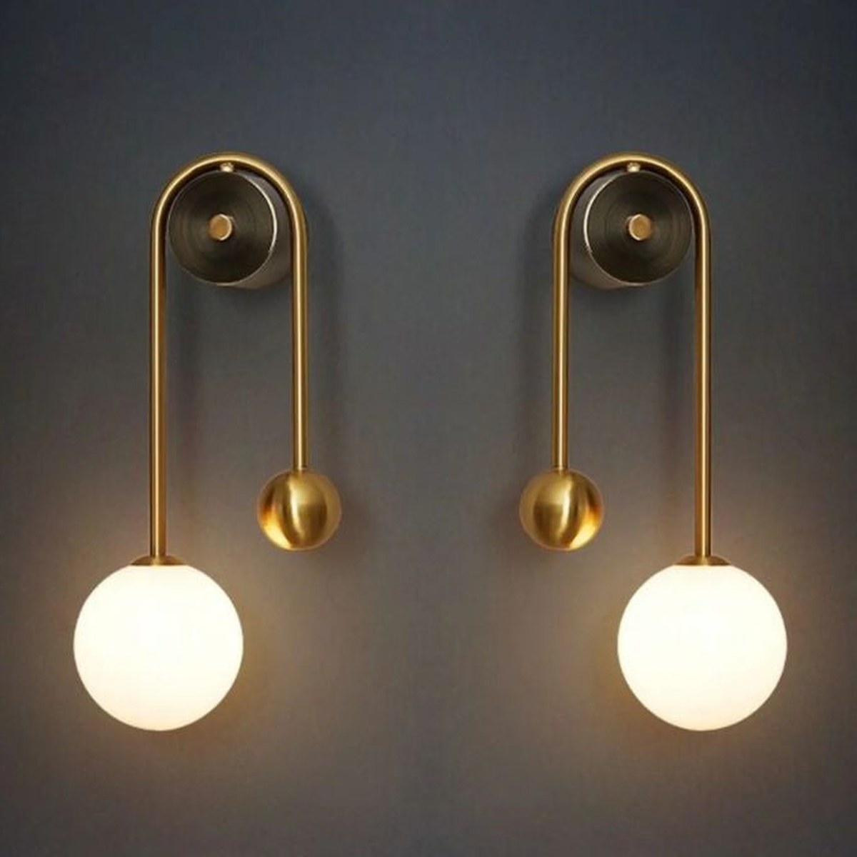 Mirrored pair of Vionessa brass wall lights with one glass globe and brass sphere